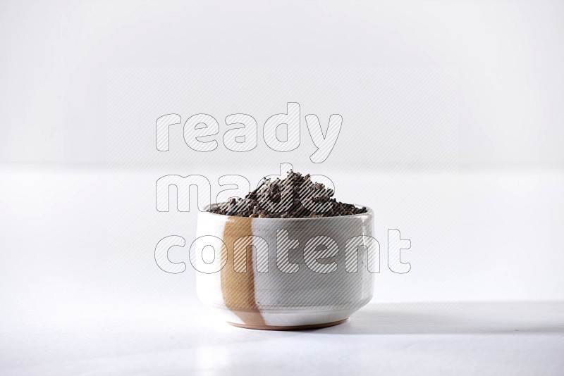 A beige ceramic bowl full of cloves on a white flooring