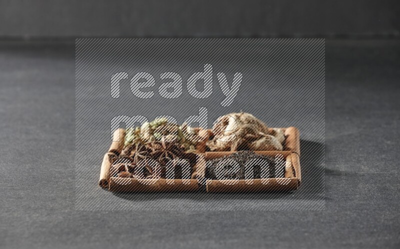 4 مربعات من عيدان القرفة ممتلئة بالشاي واليانسون النجمي والزنجبيل المجفف وحب الهيل على أرضية سوداء