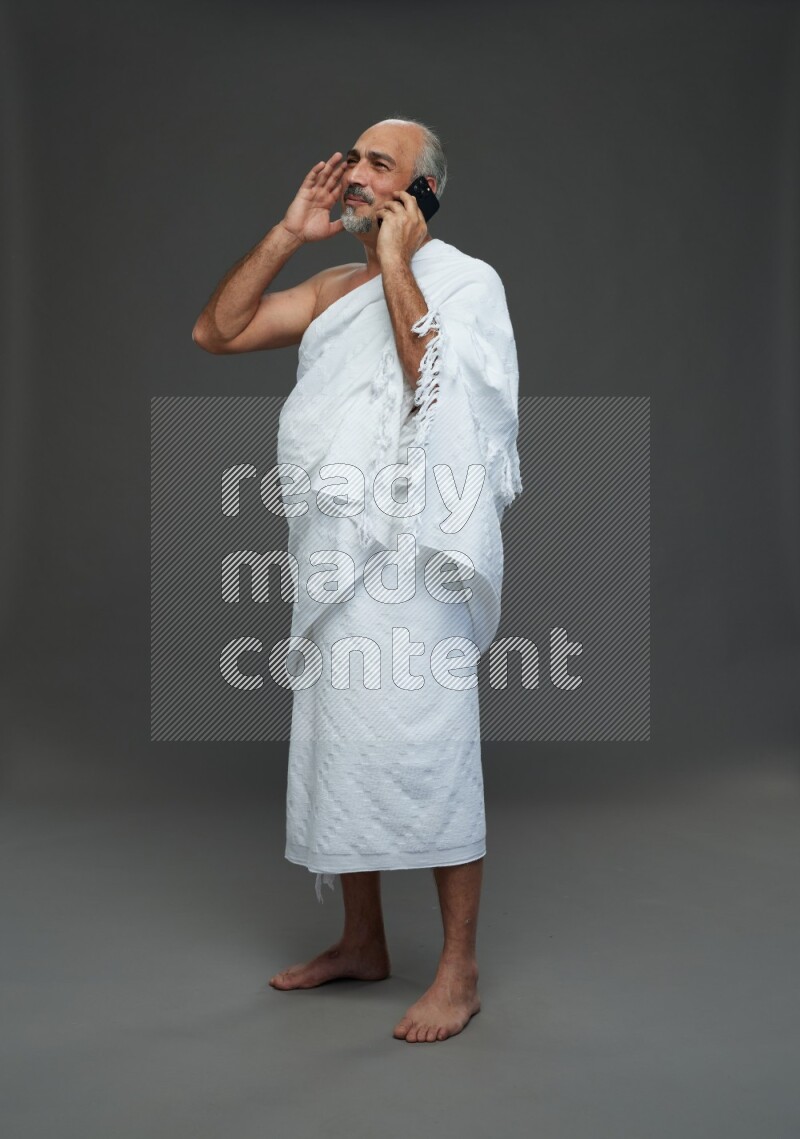 A man wearing Ehram Standing talking on phone on gray background