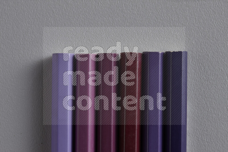 A collection of colored pencils arranged showcasing a gradient of purple hues on grey background