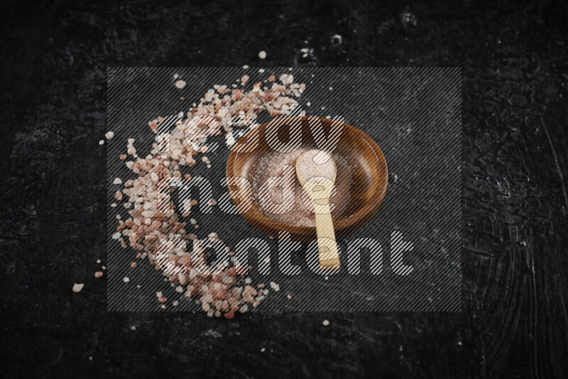 A pottery plate full of fine salt with bunch of coarse salt beside it on black background