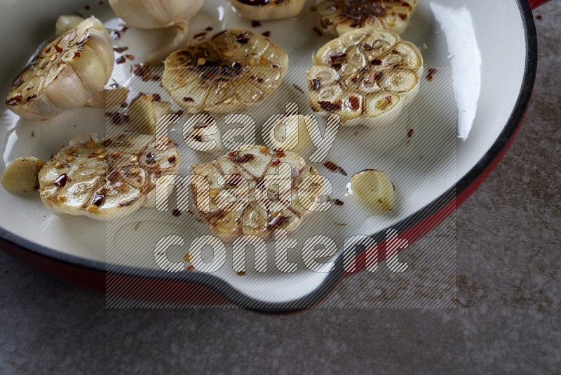 half's roasted garlic in a red-coated cast iron pan on a grey textured countertop