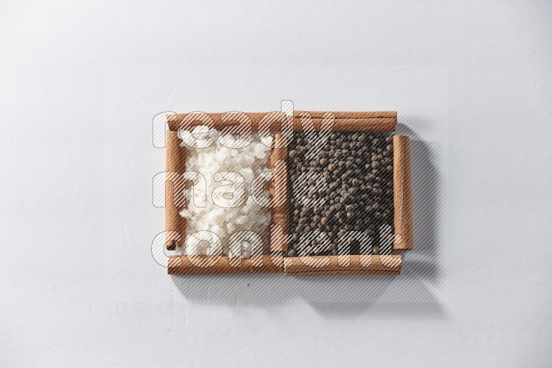 مربعان من أعواد القرفة ممتلئان بحبوب الفلفل الأسود والملح الأبيض علي خلفية بيضاء