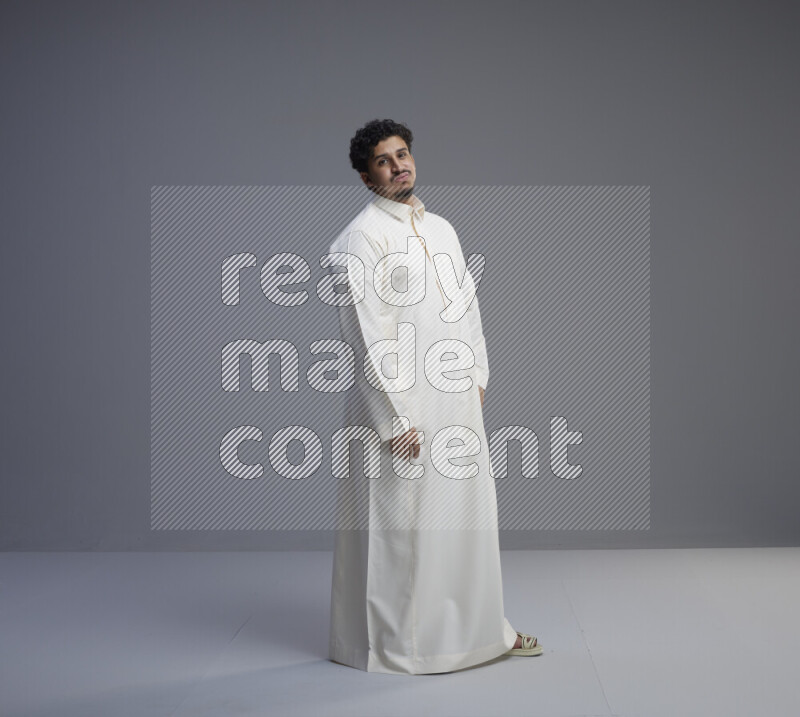 A Saudi man standing wearing thob interacting with the camera on gray background