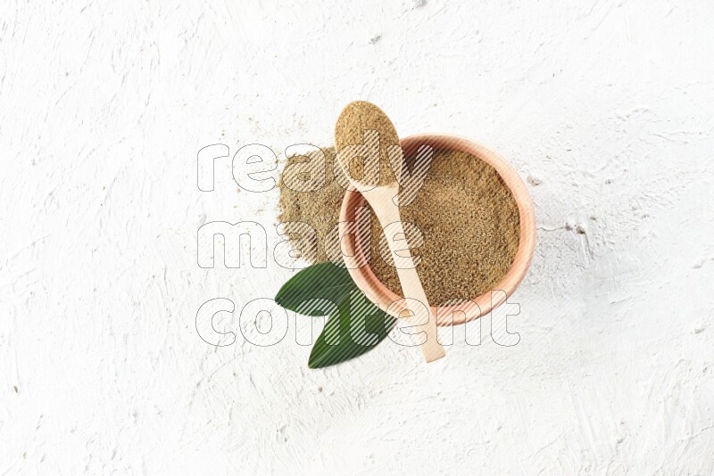 A wooden bowl and wooden spoon full of cumin powder on textured white flooring