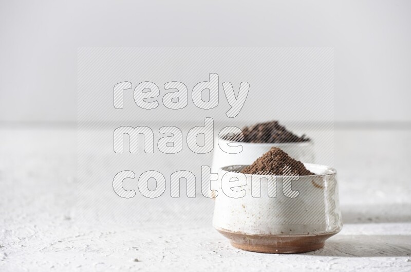 وعاءين من السيراميك بيج اللون، أحدهما مملوء بالقرنفل والآخر مملوء بالبودرة على أرضية بيضاء