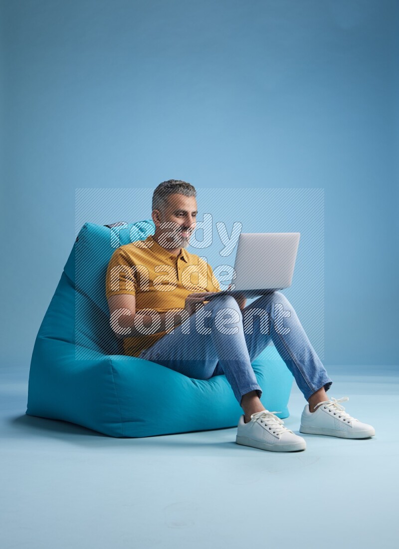 A man sitting on a blue beanbag and working on laptop