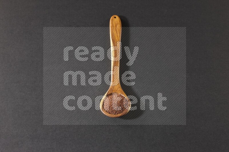 A wooden ladle full of garden cress seeds on a black flooring