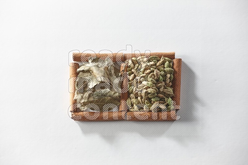 مربعان من أعواد القرفة ممتلئان بحبوب الهيل وأوراق الغار علي خلفية بيضاء