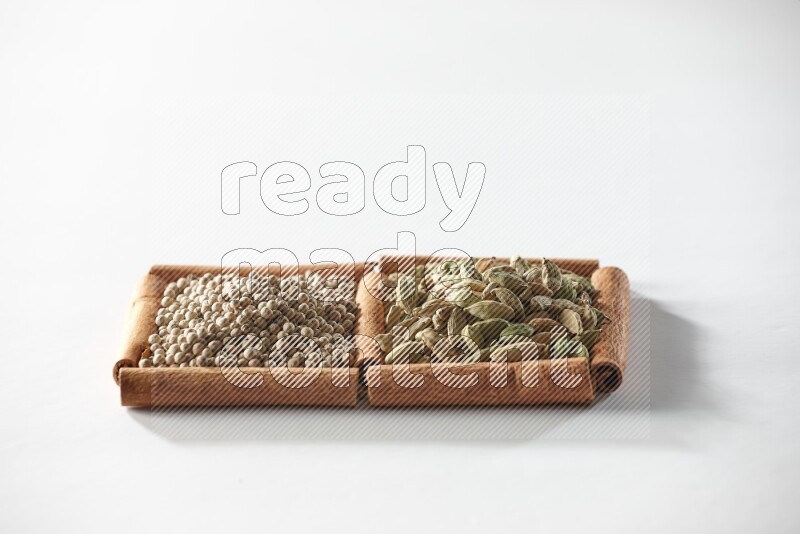 مربعان من أعواد القرفة ممتلئان بحبوب الهيل وحبوب الفلفل الأبيض علي خلفية بيضاء