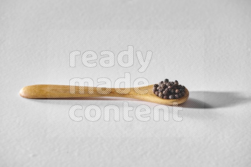 A wooden spoon full of black pepper on white flooring