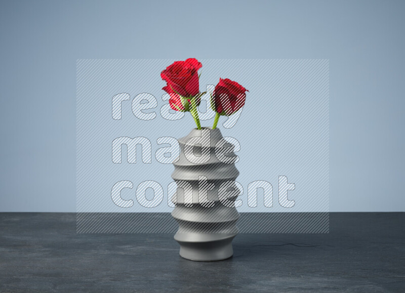 An arrangement of vivid red roses in a grey spiral vase on black marble background
