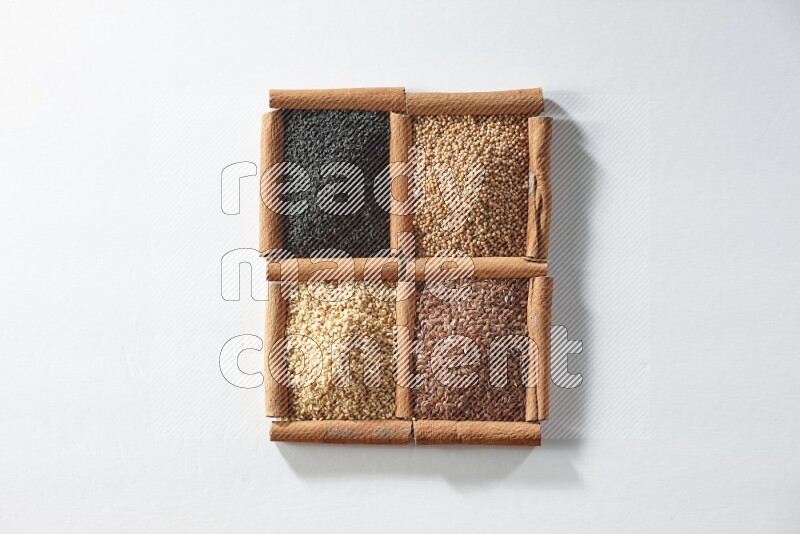 4 مربعات من أعواد القرفة ممتلئة بحبة البركة وبذور الخردل وبذور الكتان والسمسم على أرضية بيضاء