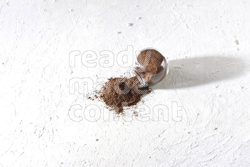 A flipped glass spice jar full of cloves powder and powder came out of it on textured white flooring