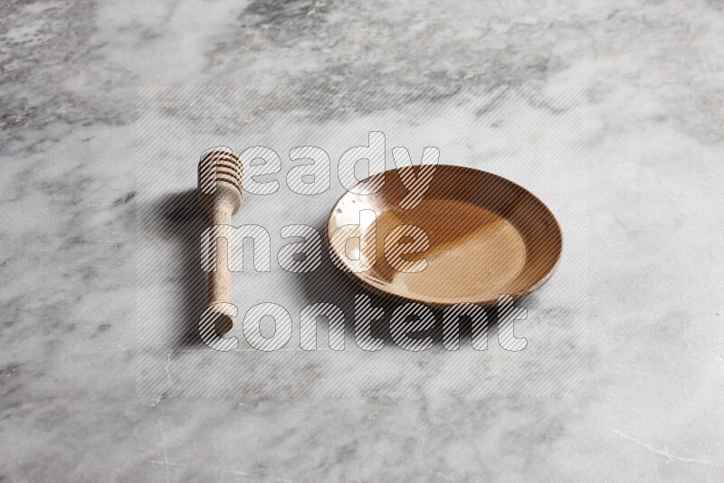 Multicolored pottery plate with wooden honey dipper on the side on grey marble background