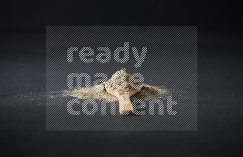 ملعقة خشبية ممتلئة ببودرة الهيل والبودرة تناثرت على خلفية سوداء