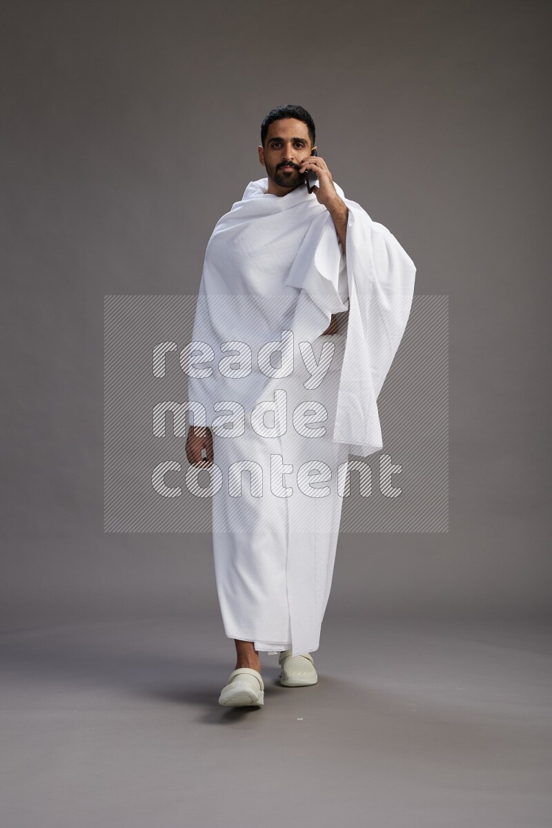 A man wearing Ehram Standing talking on phone on gray background