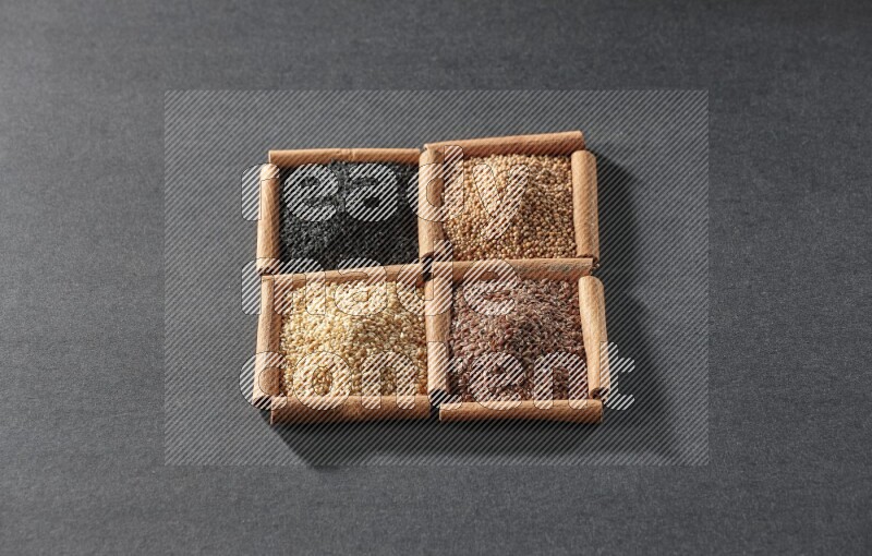 4 مربعات من عيدان القرفة ممتلئة بحبة البركة السوداء وبذور السمسم وبذور الكتان وحبوب الخردل على أرضية سوداء