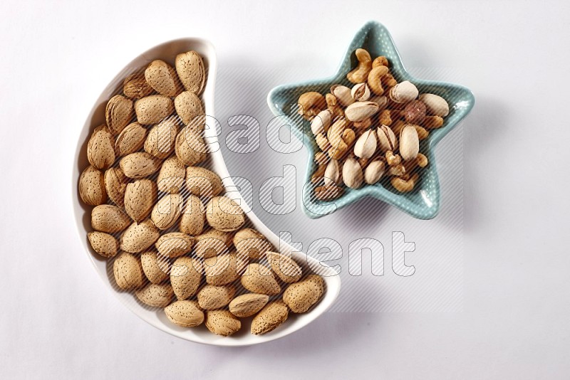 Almonds in a crescent pottery plate and a star shaped plate with mixed nuts on white background