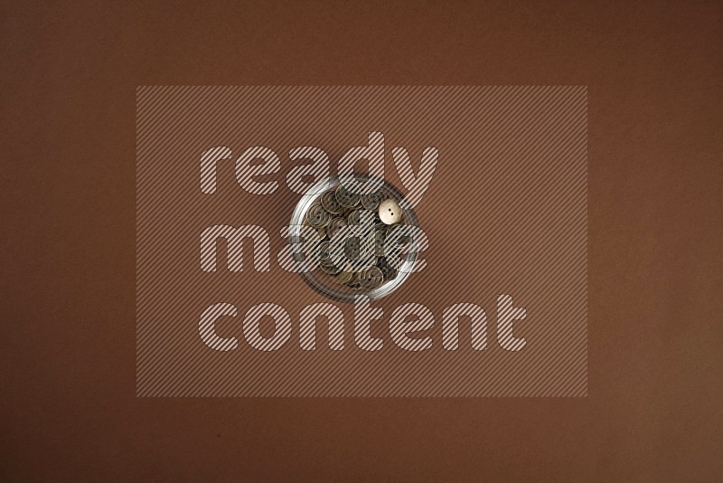 A glass bowl full of brown buttons on brown background