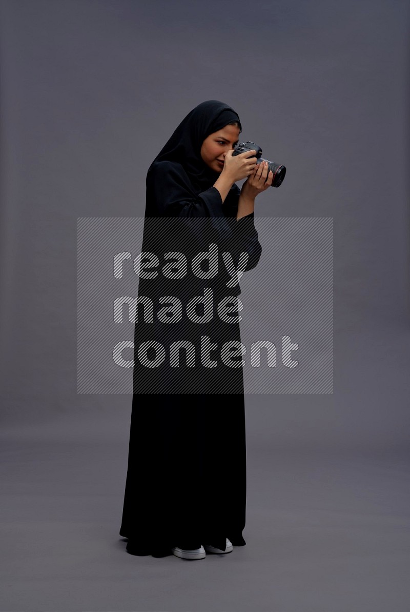 Saudi woman wearing Abaya standing holding Camera on gray background