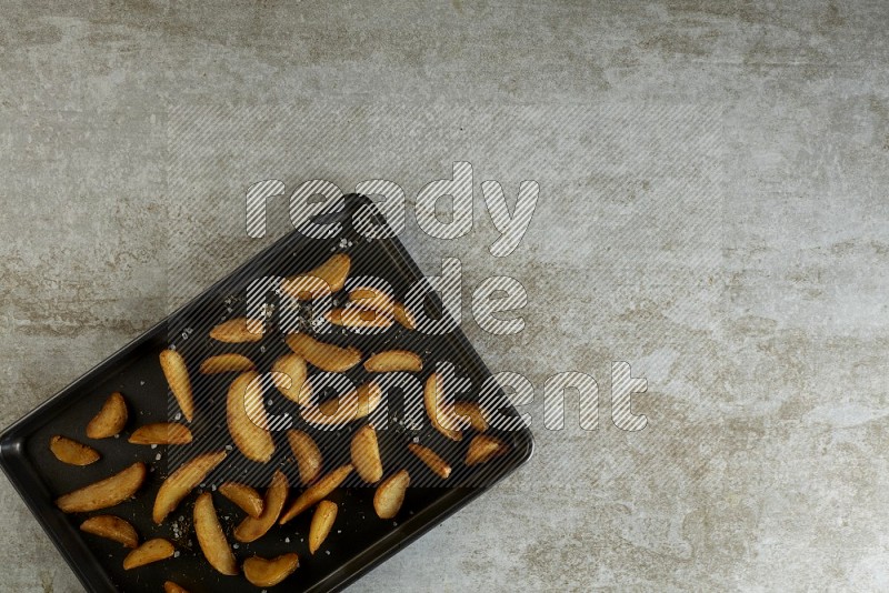wedges potato in a black stainless steel rectangle tray on grey textured counter top
