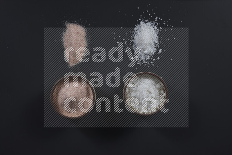 2 وعاء فخاري احدهمها ممتلئ بملح الهيمالايا والأخر بالملح الأبيض على خلفية سوداء