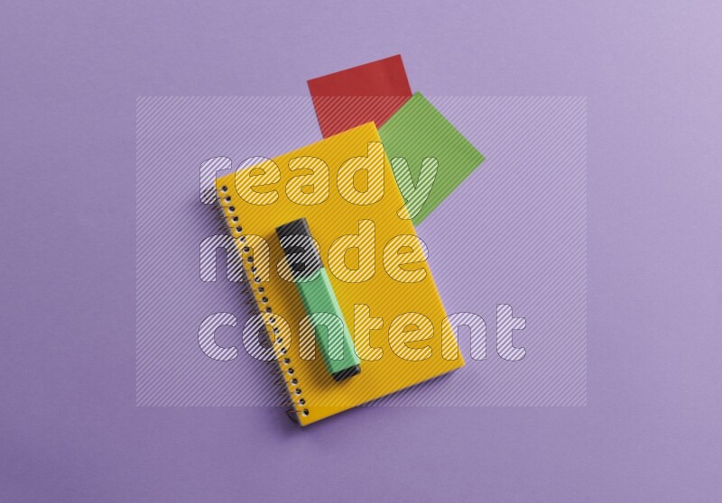 A yellow notebook with school supplies on purple background