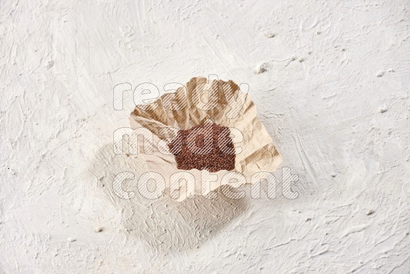 A crumpled piece of paper full of garden cress seeds on a textured white flooring
