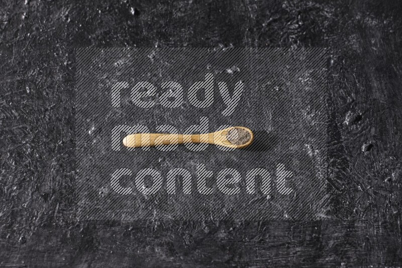 حبوب الفلفل الأسود في ملعقة خشبية علي خلفية سوداء