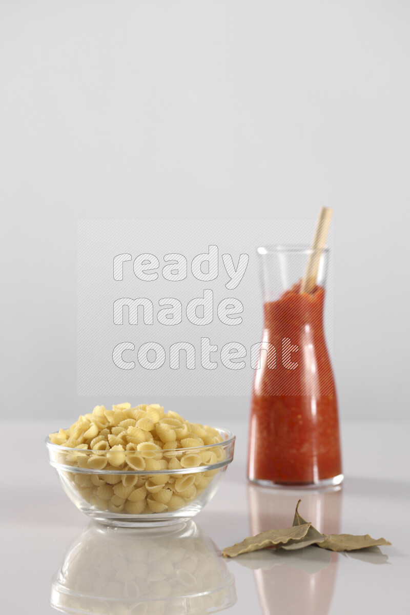 Raw pasta with tomatoe pasta with different ingredients such as cherry tomatoes, basil, garlic, bay laurel, cardamom, white pepper, black pepper, red chilis and wheat stalks on light grey background