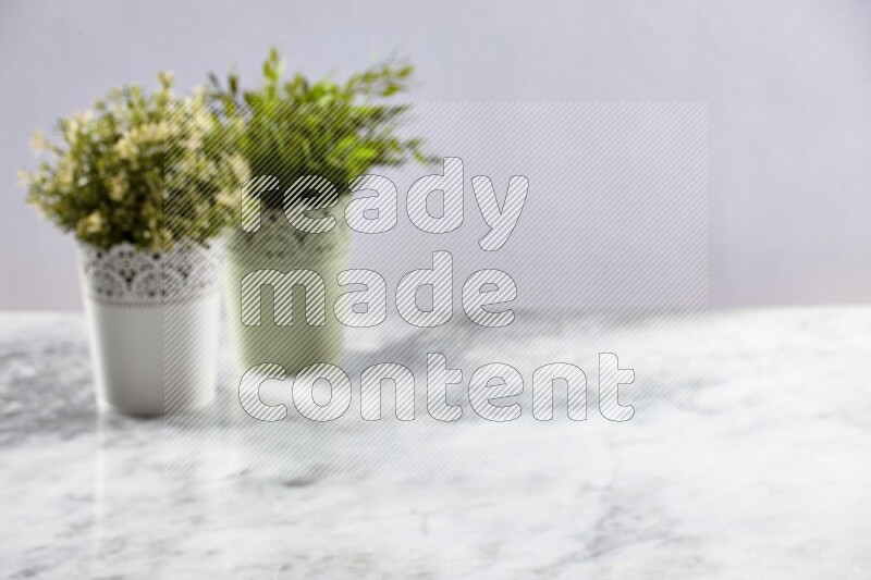 Two different artificial plants in white and green decorative pot on grey marble background
