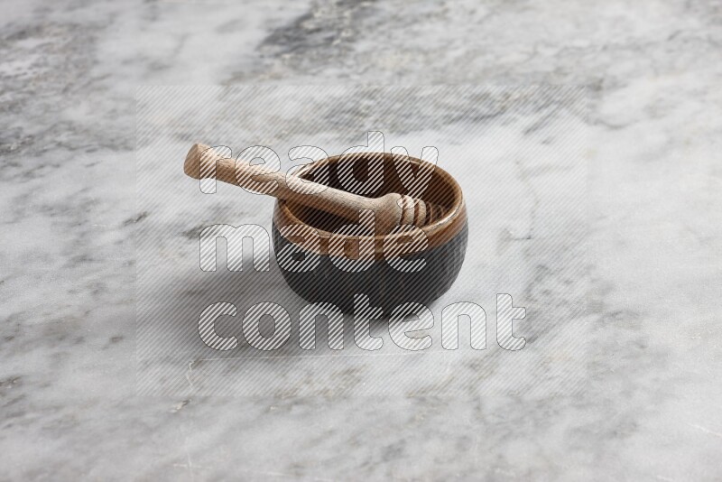 Multicolored pottery bowl with wooden honey dipper in it on grey marble background