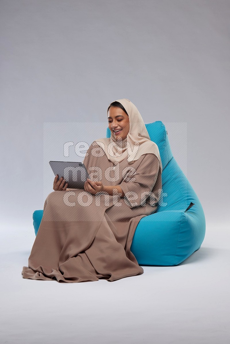 A Saudi woman sitting on a blue beanbag and working on tablet