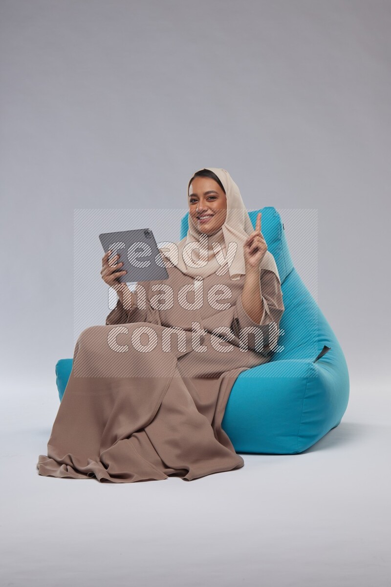 A Saudi woman sitting on a blue beanbag and working on tablet