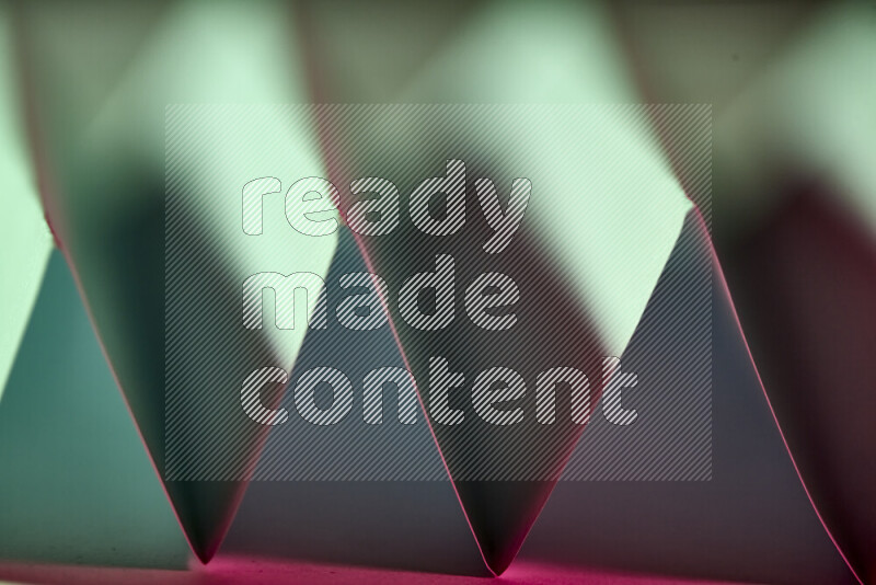 A close-up abstract image showing sharp geometric paper folds in green and pink gradients
