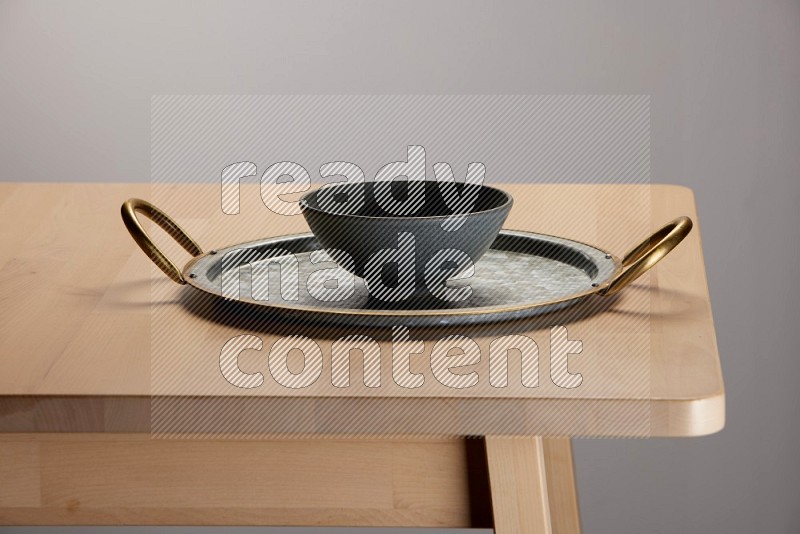 grey bowl placed on a rounded stainless steel tray with golden handels on the edge of wooden table