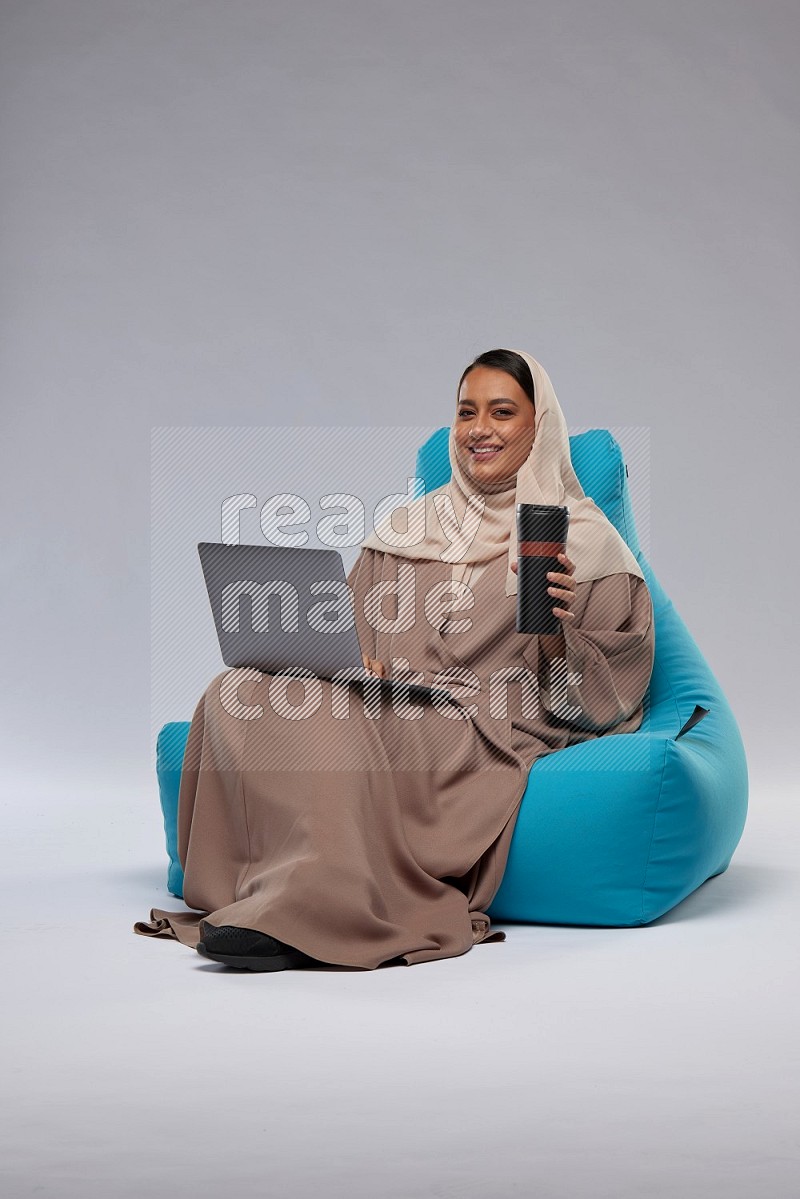 A Saudi woman sitting on a blue beanbag and working on laptop