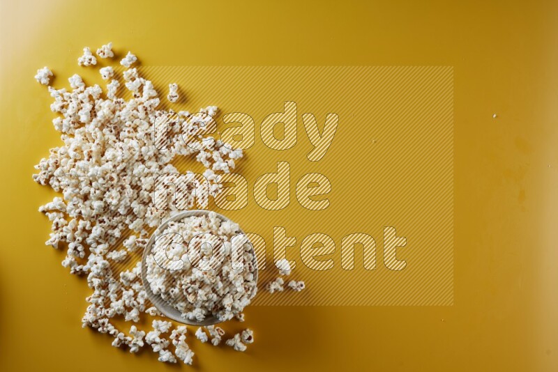 A white pottery bowl full of popcorn with popcorn beside it on a yellow background in different angles