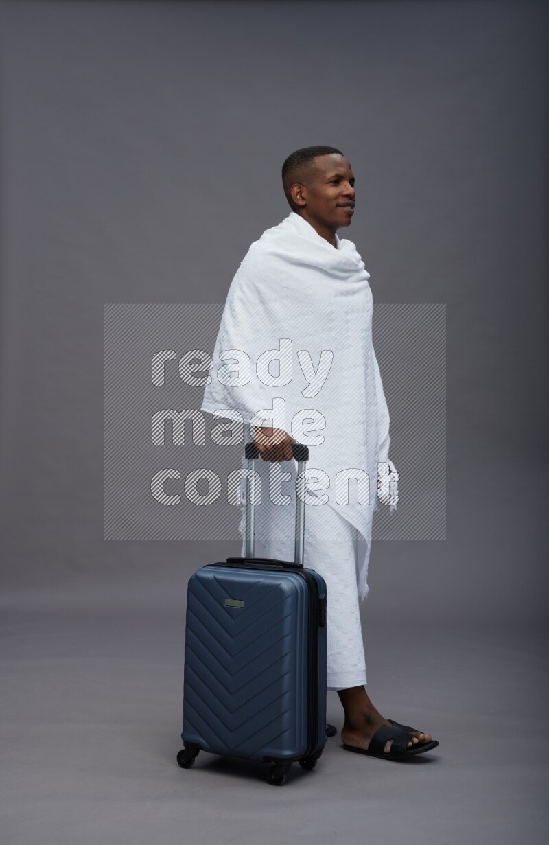 A man wearing Ehram Standing holding traveling bag on gray background