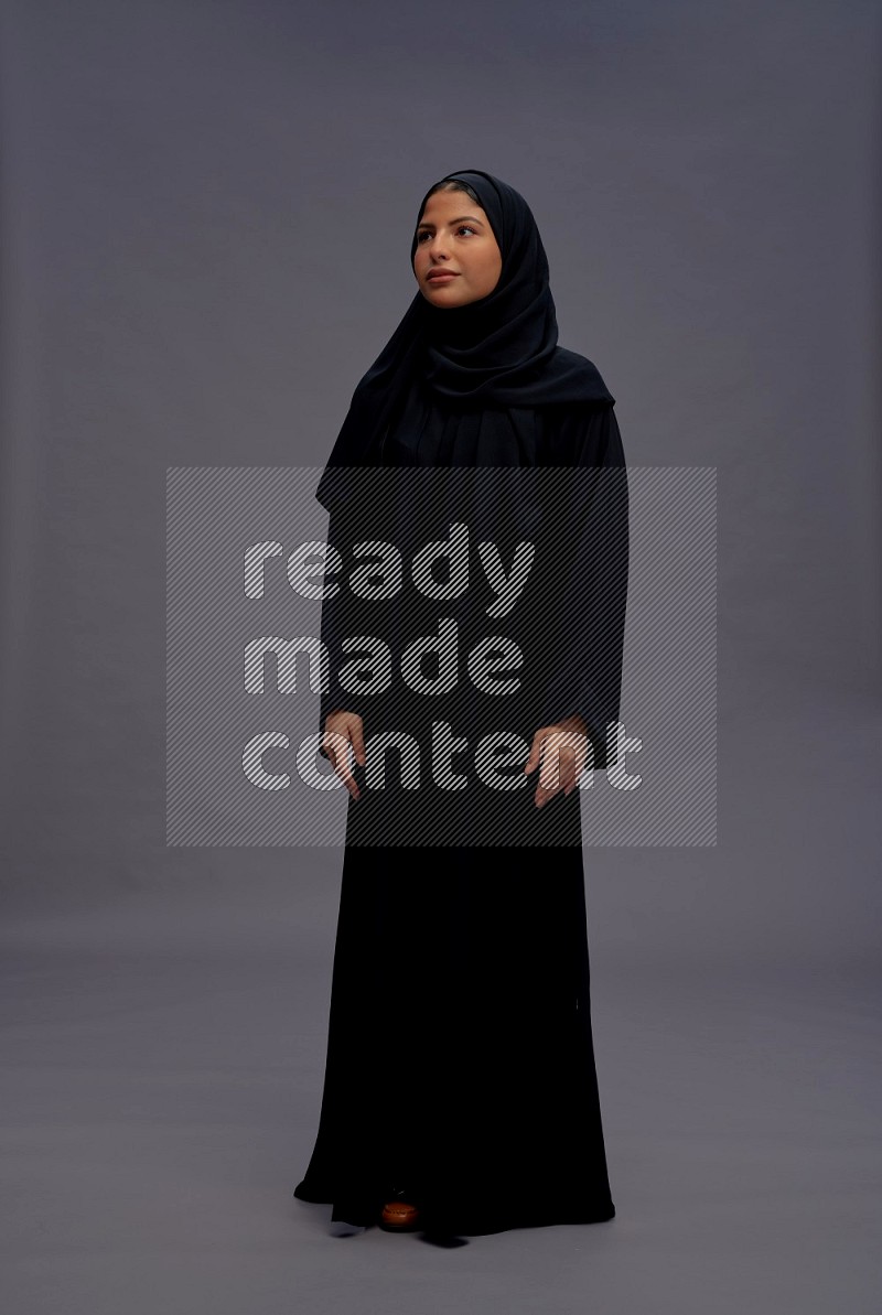 Saudi woman wearing Abaya standing interacting with the camera on gray background