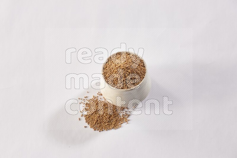 A beige pottery bowl full of mustard seeds and more seeds spread on a white flooring