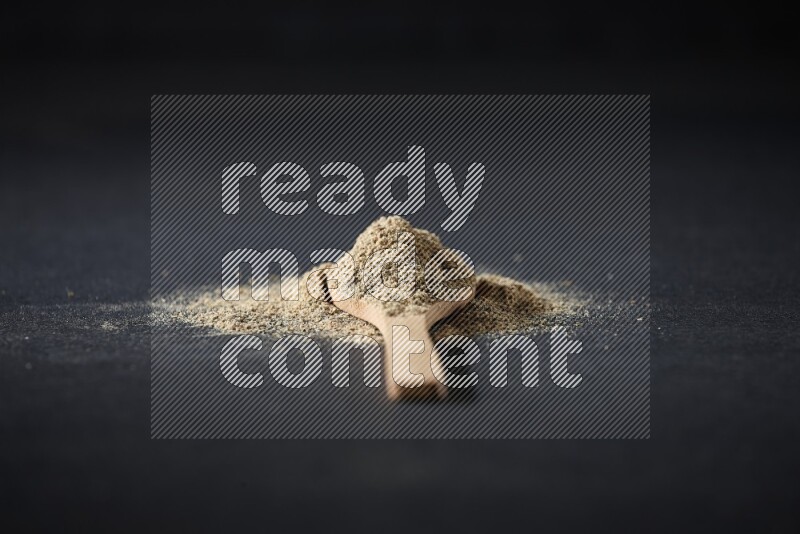 ملعقة خشبية ممتلئة ببودرة الهيل والبودرة تناثرت على خلفية سوداء