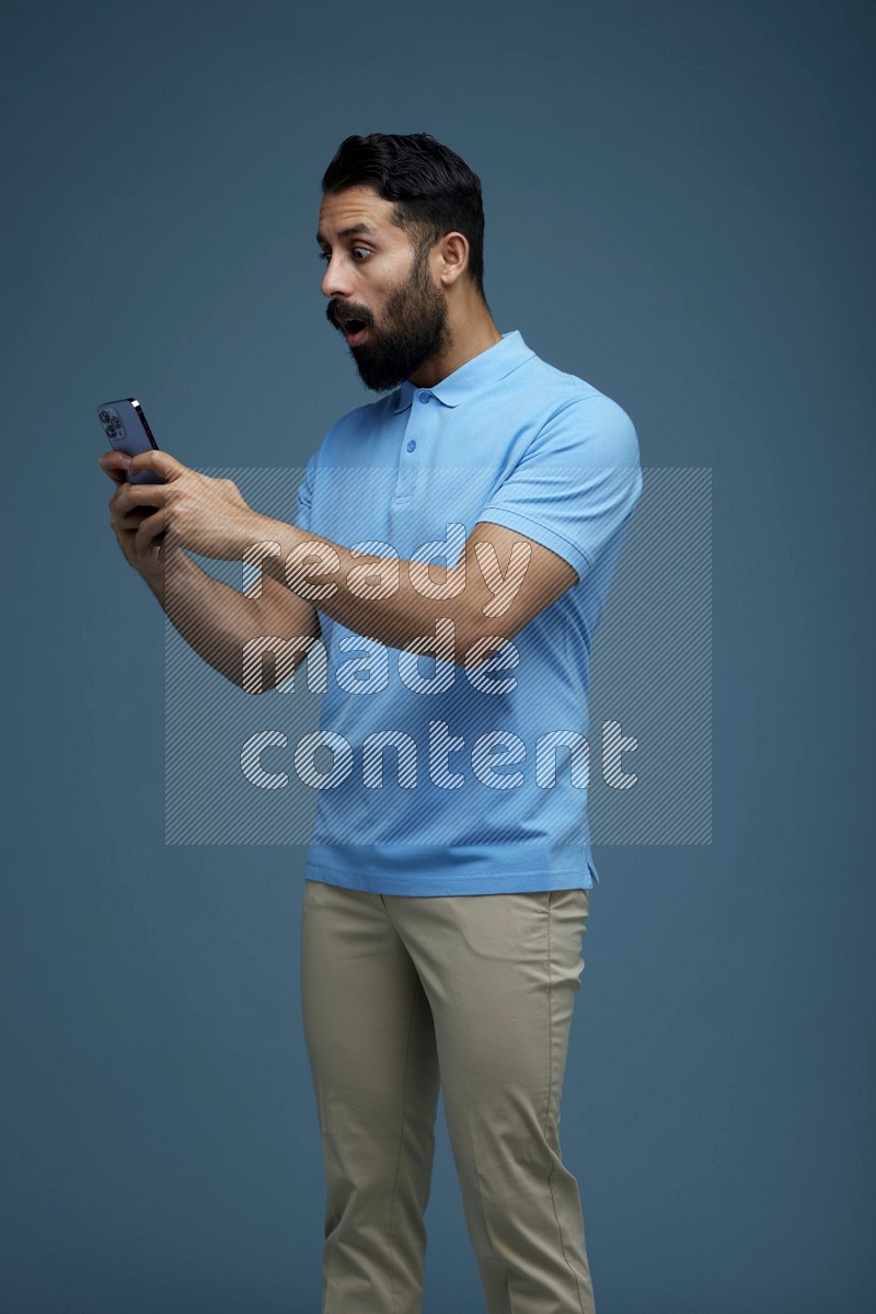 A man Texting on his phone in a blue background wearing a Blue shirt