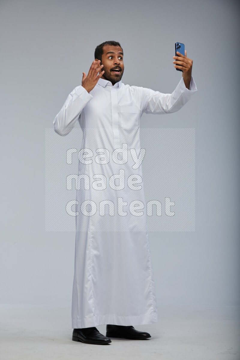 Saudi man wearing Thob standing taking selfie on Gray background