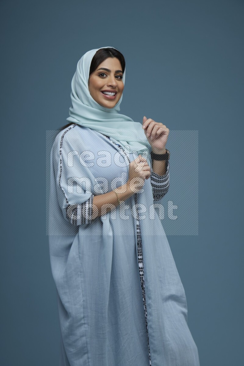 A woman posing in a blue background wearing a blue Abaya with hijab