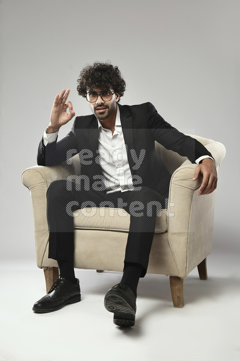 A man wearing formal sitting on a chair making a hand gesture on white background
