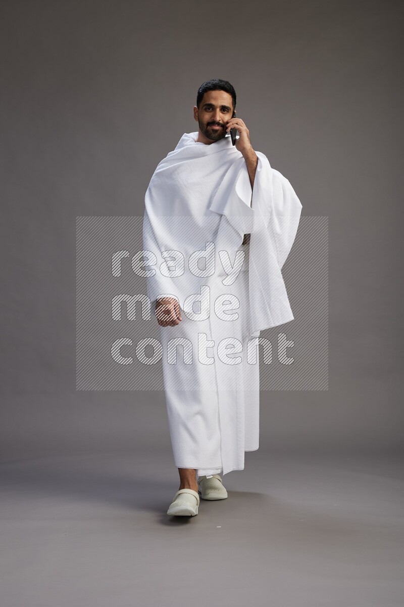 A man wearing Ehram Standing talking on phone on gray background