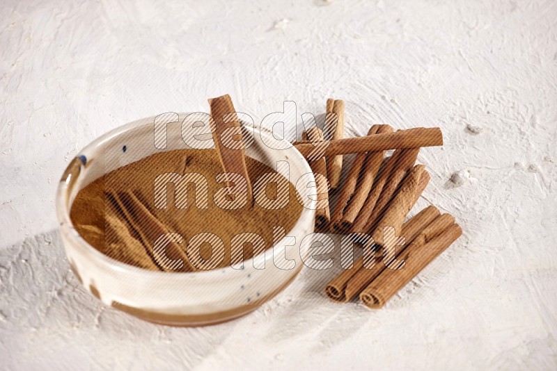 Ceramic bowl full of cinnamon powder and pieces of sticks with cinnamon sticks on the side on white background in different angles