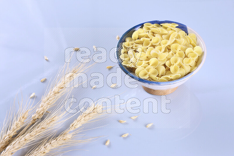 Raw pasta with wheat stalks on light blue background